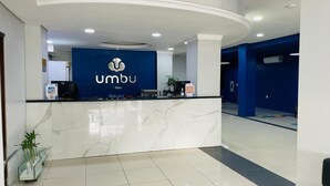 A reception area with a marble counter, a blue wall with the logo 'umbu', and a potted plant. - Umbu Hotel Porto Alegre (Porto Alegre)