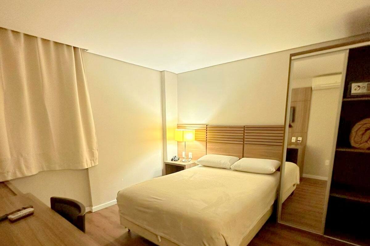 A hotel room with a bed, bedside table, lamp, and a mirror.