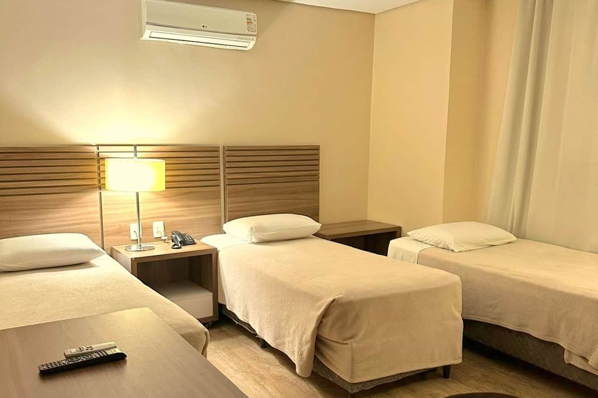 A hotel room with two single beds, a desk, a chair, a lamp, a phone, and a remote control.