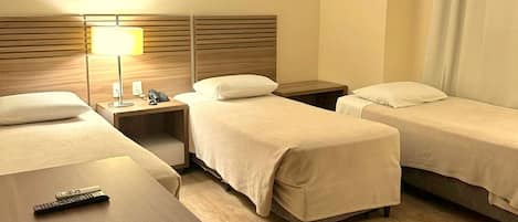 Une chambre d’hôtel avec deux lits simples, un bureau, une chaise, une lampe, un téléphone et une télécommande.