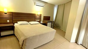 A hotel room with a large bed, bedside tables, a nightstand, an air conditioning unit, and a curtain on the window. - Umbu Hotel Porto Alegre (Porto Alegre)
