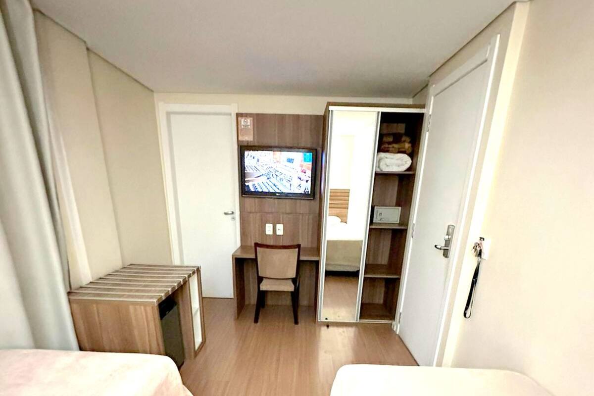 A hotel room with two beds, a desk, a chair, a TV, and a wardrobe.