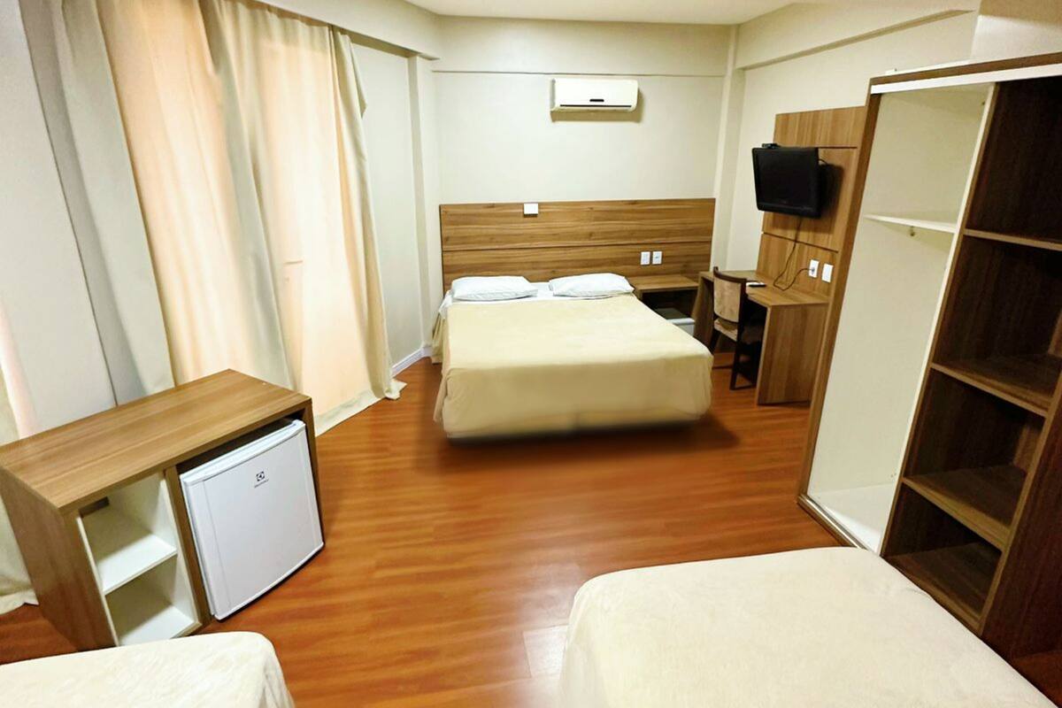 A hotel room with a bed, a desk with a chair, a wardrobe, and a television.