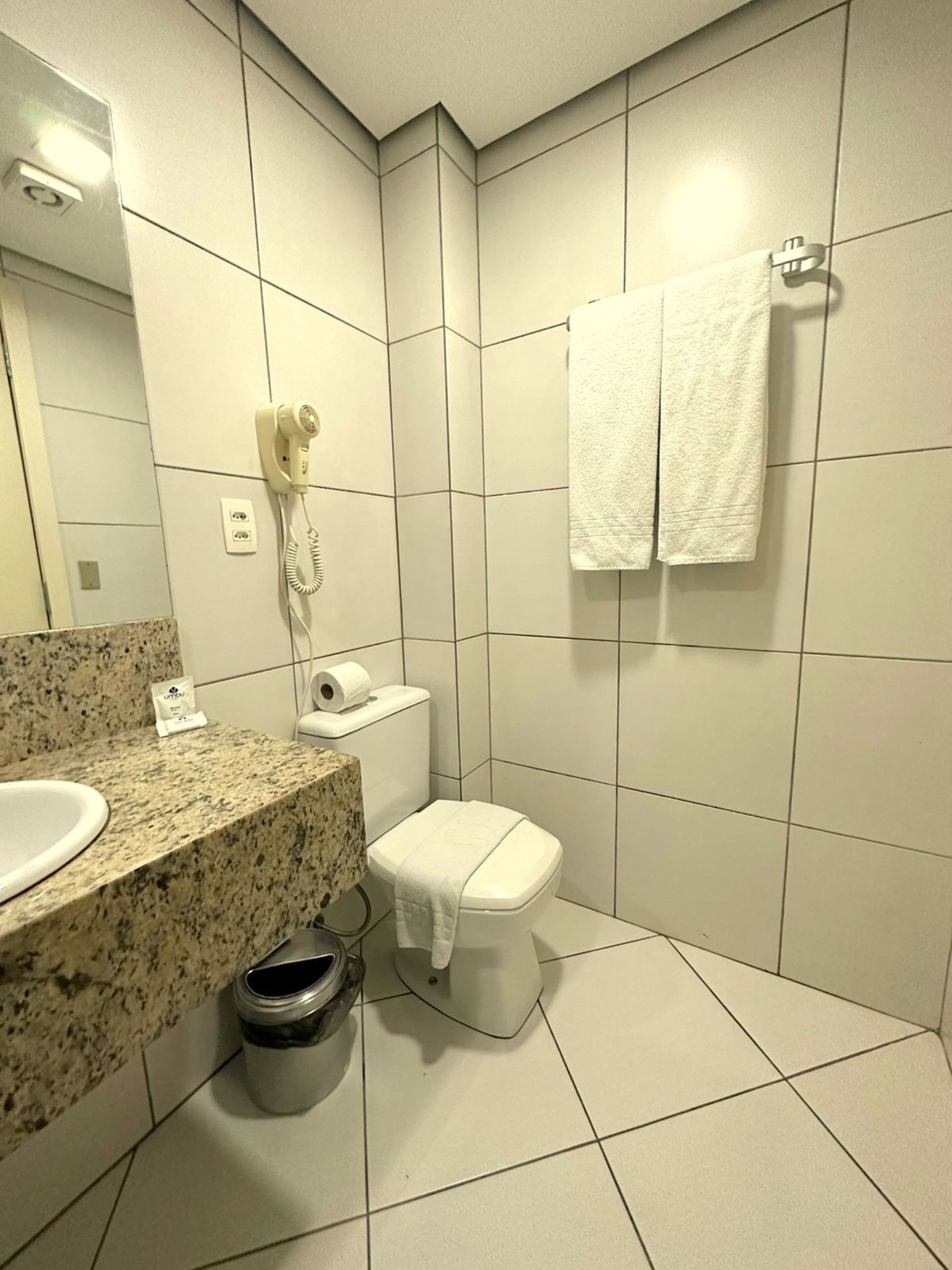 A modern bathroom with a granite countertop, a toilet, a hairdryer, and a towel rack.
