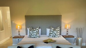 Una habitación de hotel con una cama grande, dos mesitas de noche con lámparas, dos sillones y un jarrón decorativo.