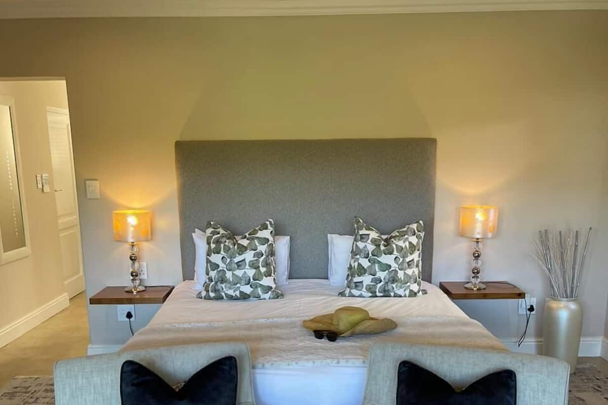 A hotel room with a large bed, two bedside tables with lamps, two armchairs, and a decorative vase.