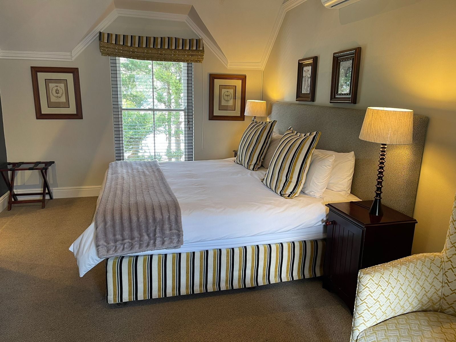A neatly made bed with striped bedding, a bedside lamp, and framed pictures on the wall.