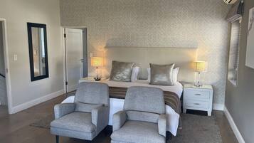 A hotel room with a bed, two armchairs, a nightstand, a mirror, and patterned wallpaper.