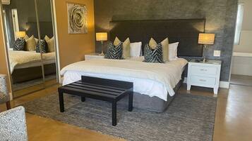 Um quarto moderno com uma cama grande, mesas de cabeceira, um banquinho e um espelho.