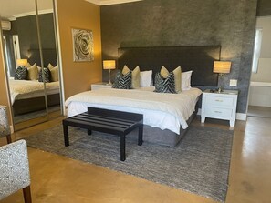 Ein modernes Schlafzimmer mit einem großen Bett, Nachttischen, einer Bank und einem Spiegel.