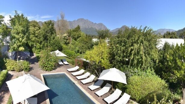 Zona de piscina con sillones de descanso y sombrillas, rodeada de exuberante vegetación y montañas al fondo.