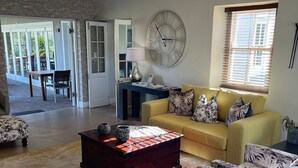 Un salón amplio con un sofá amarillo, sillones estampados, una mesa de centro de madera y un reloj de pared grande.