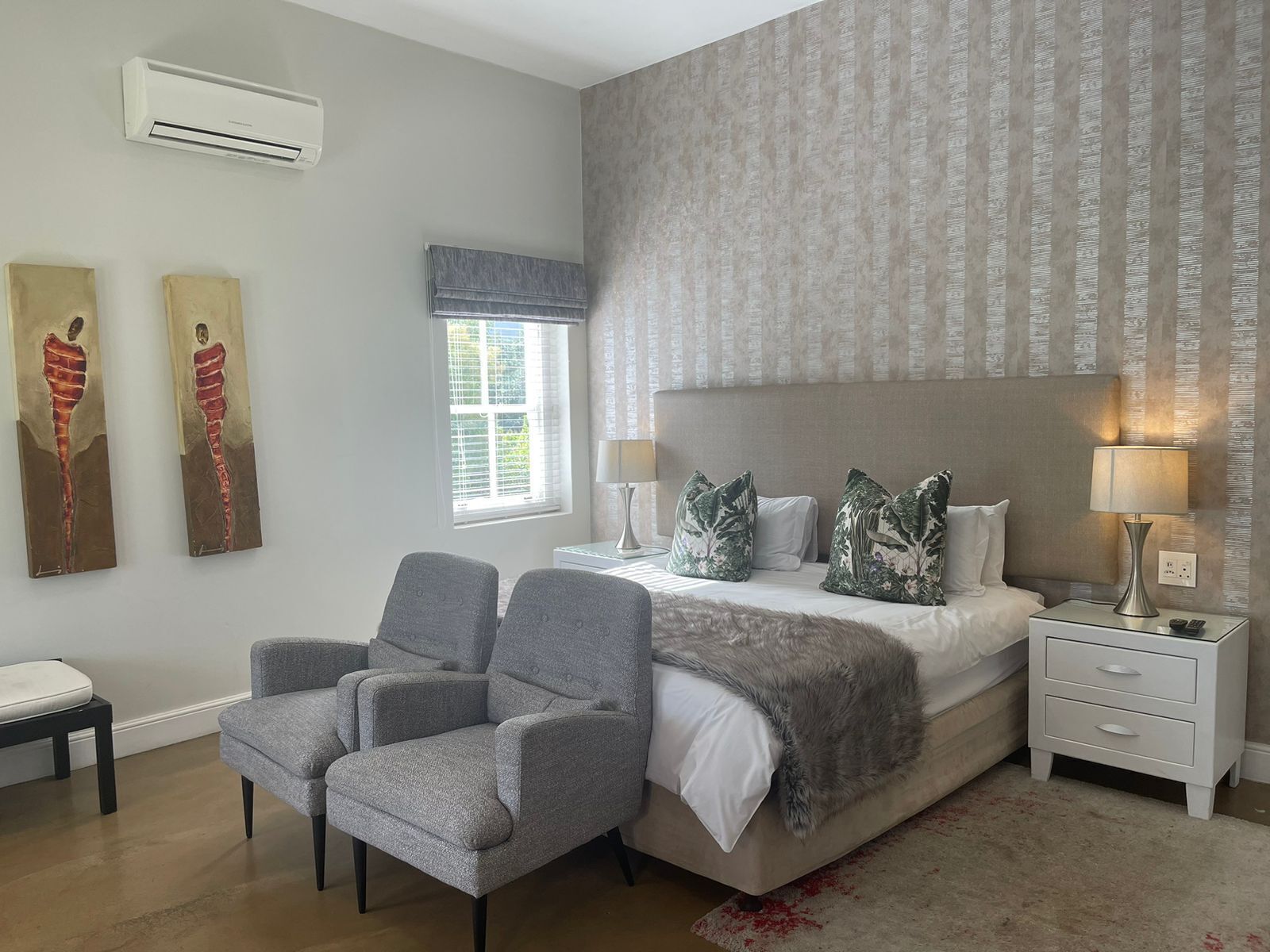 A bedroom with a bed, two chairs, a nightstand, a lamp, and artwork on the wall.