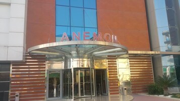 La entrada de un hotel con fachada de vidrio y el nombre 'ANEMON' exhibido sobre la entrada.