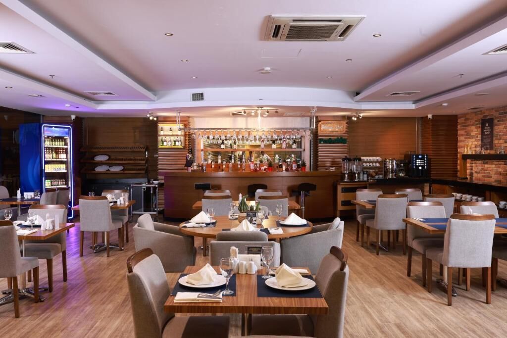 A restaurant with a bar area, tables set for dining, and a variety of bottles on shelves.