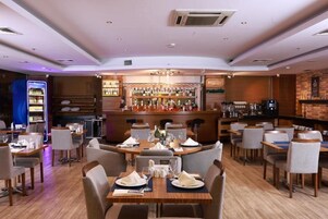 A restaurant with a bar area, tables set for dining, and a variety of bottles on shelves.