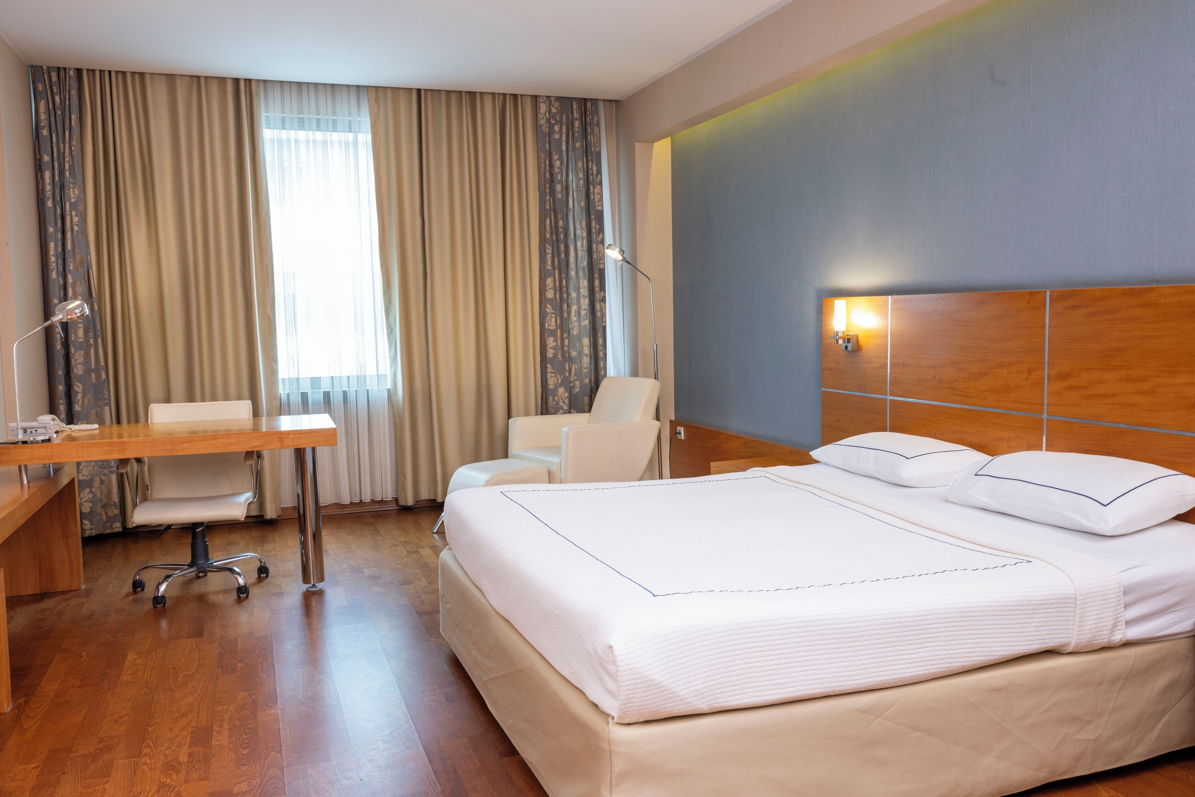 A hotel room with a large bed, a desk, a chair, and a lamp.