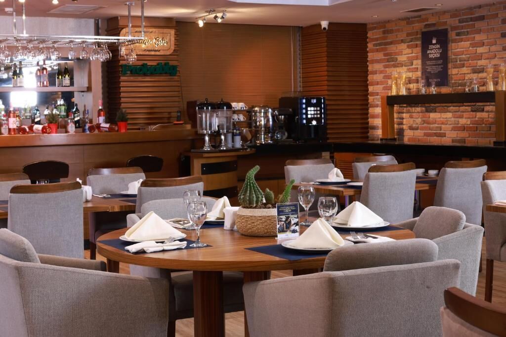 A restaurant with round tables, chairs, a bar area, and a brick wall.