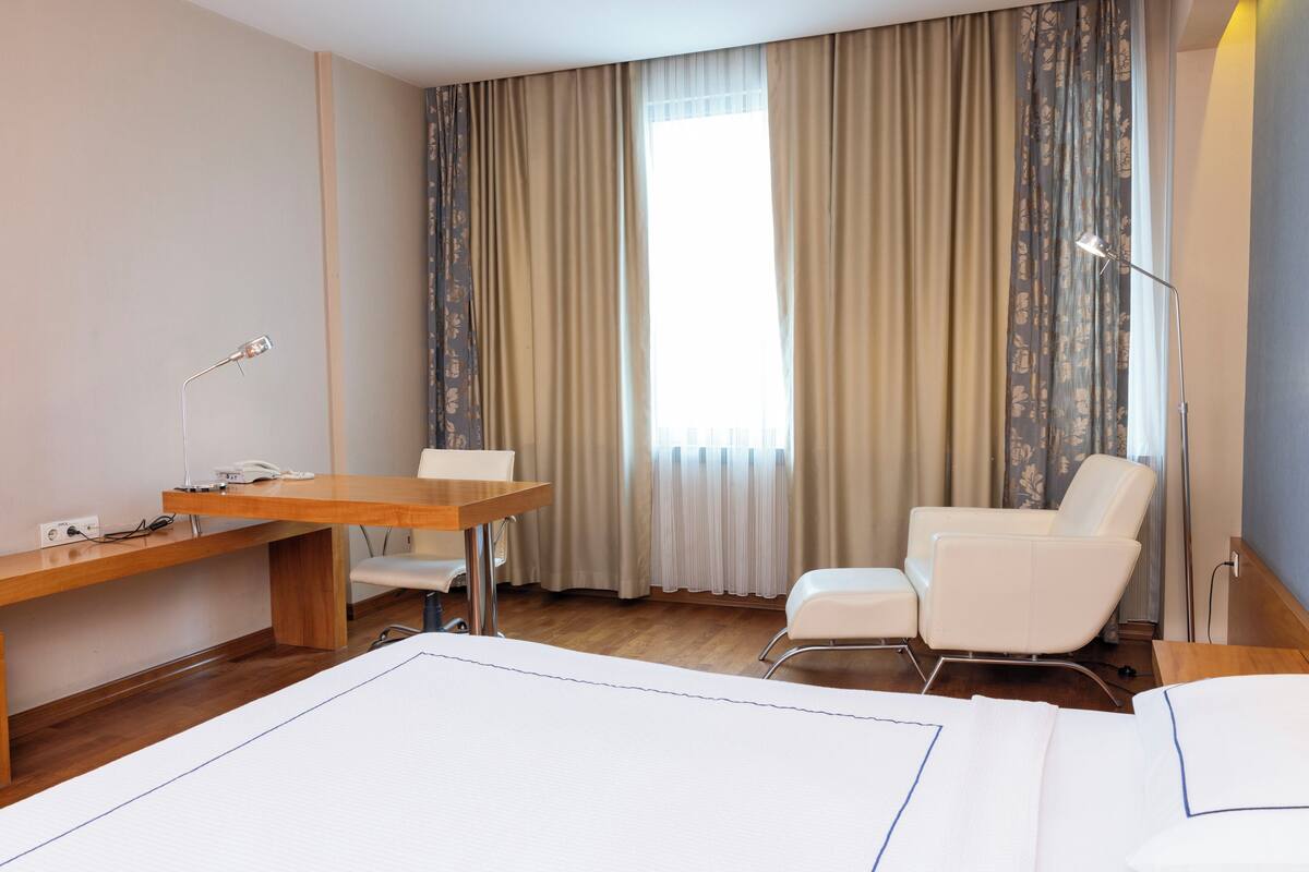 A hotel room with a bed, a desk, a chair, and a lamp.