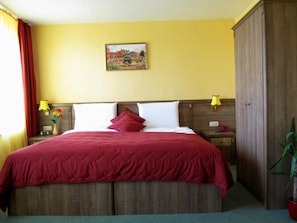 Una habitación de hotel con cama, mesita de noche, lámpara, armario y un cuadro en la pared.