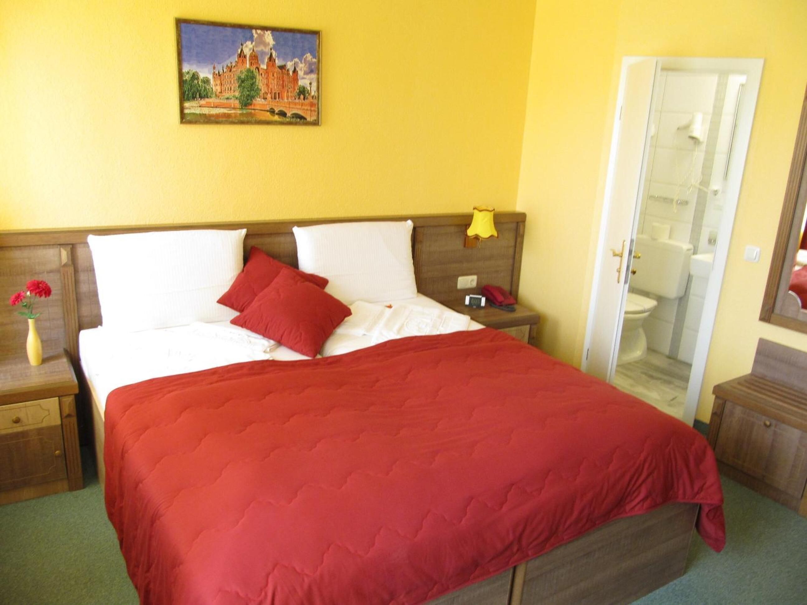 Habitación de hotel con cama, mesita de noche, un cuadro en la pared y la puerta del baño.
