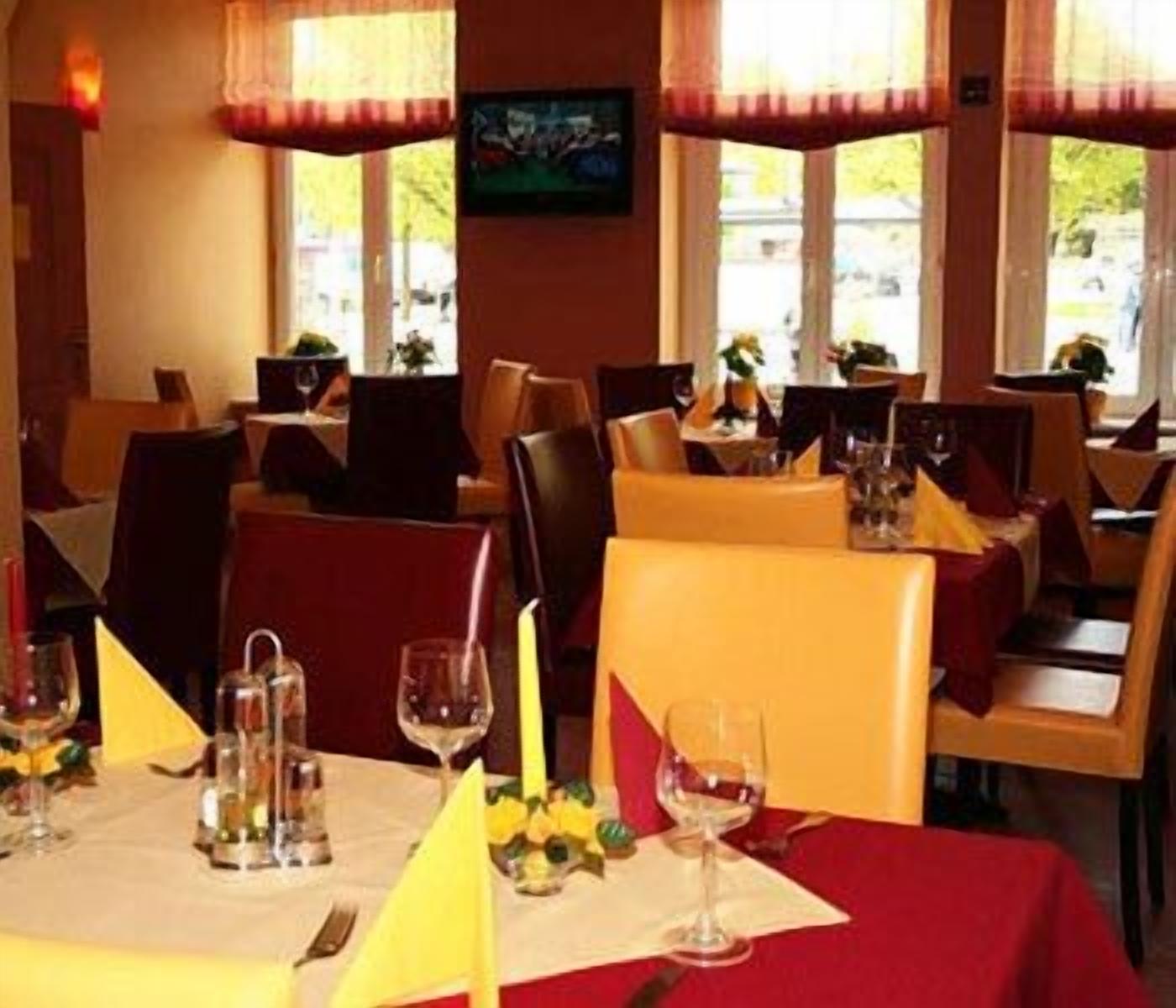 A restaurant interior with tables set for dining, chairs, and a television screen on the wall.