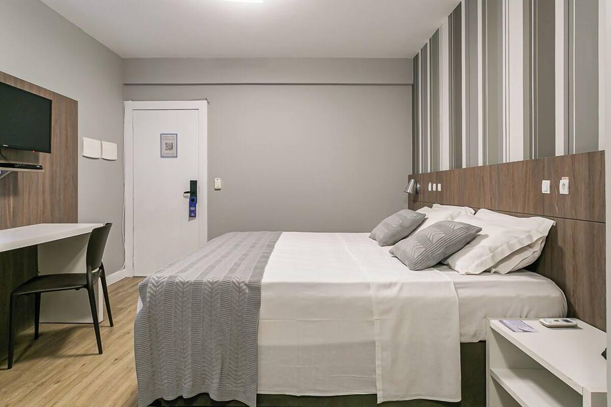 Una habitación de hotel moderna con una cama, un escritorio y un televisor montado en la pared.