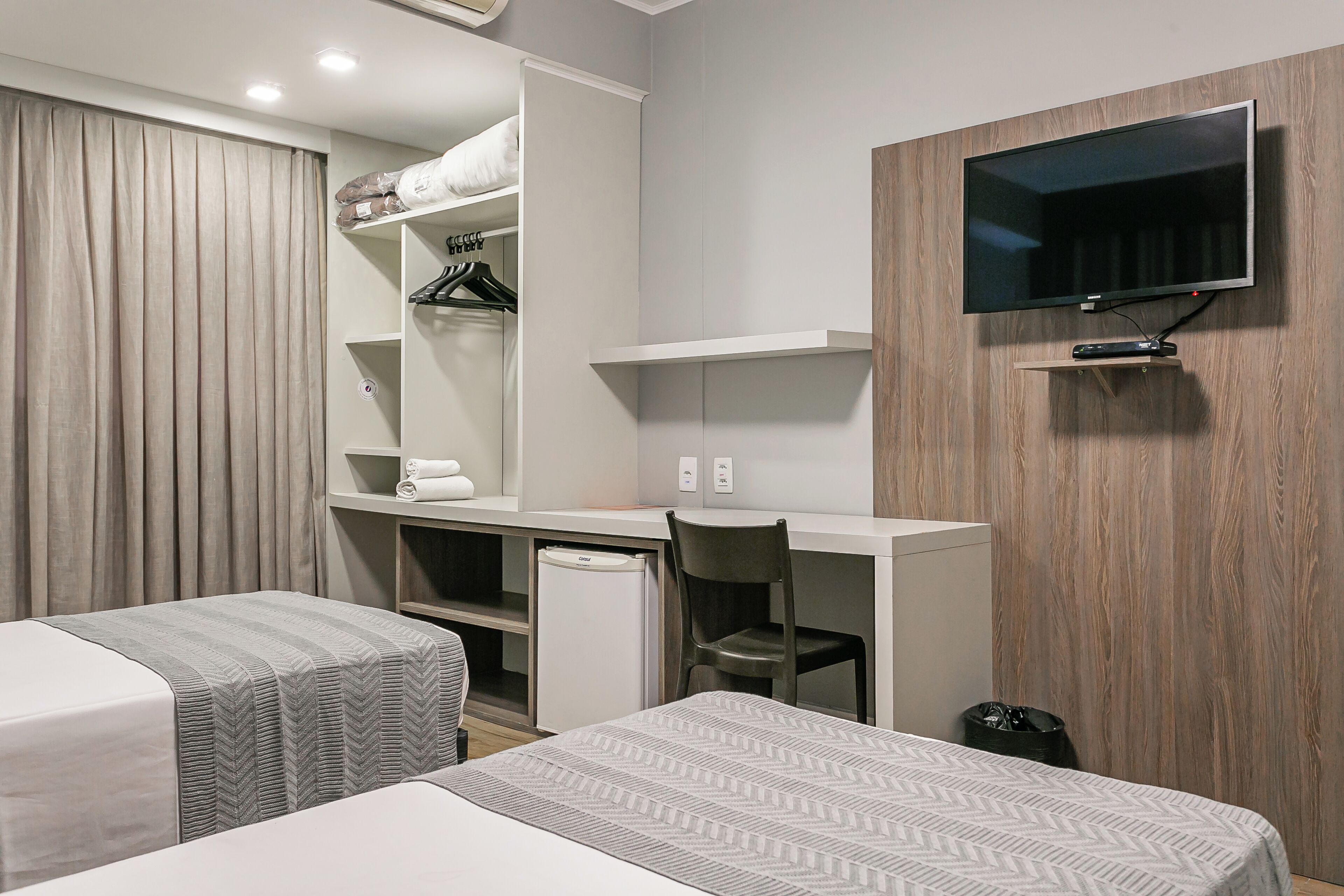 Ein Hotelzimmer mit zwei Betten, einem Schreibtisch, einem Stuhl, einem Fernseher und einem Kleiderschrank.
