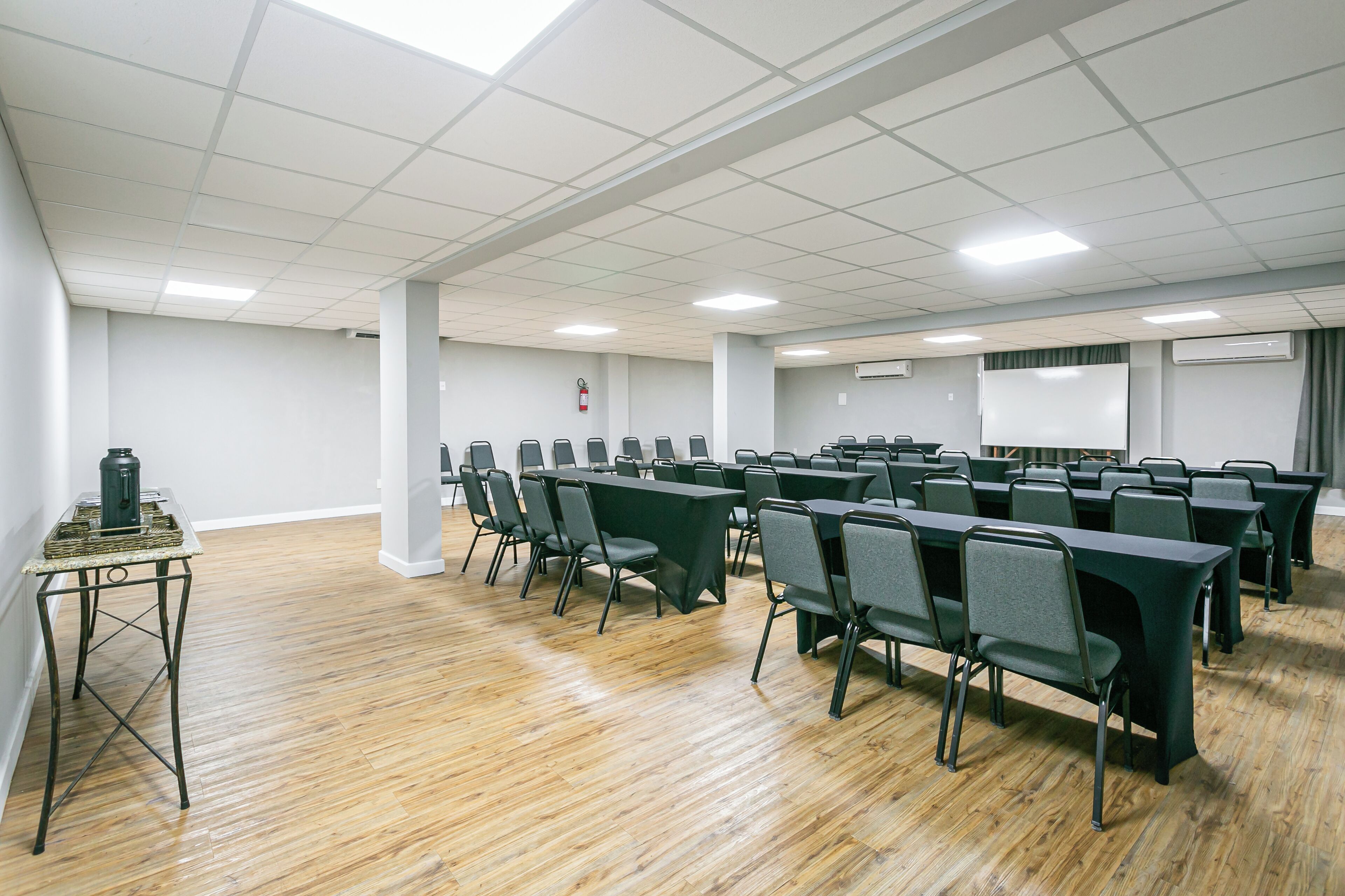 Un salón de conferencias con una larga mesa y sillas, una mesa pequeña con una lámpara, y una pizarra.