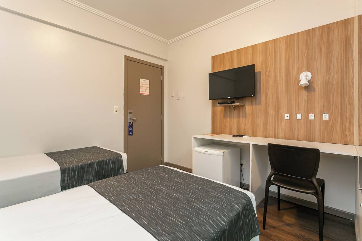 Habitación de hotel con dos camas, un escritorio, una silla, un televisor y un refrigerador pequeño.