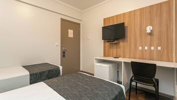 A hotel room with two beds, a desk, a chair, a TV, and a small refrigerator.