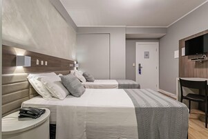 A hotel room with two beds, a desk, a chair, and a TV mounted on the wall.