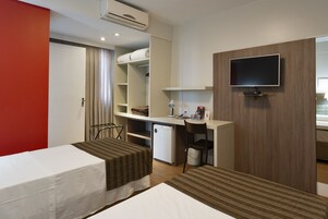 A hotel room with two beds, a desk, a television, and a mini-fridge.