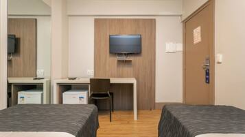 Ett hotellrum med två sängar, ett skrivbord, en stol, en tv som är monterad på väggen och en dörr med en skylt.