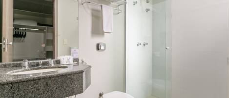A modern bathroom with a granite countertop sink, a toilet, and a glass-enclosed shower.