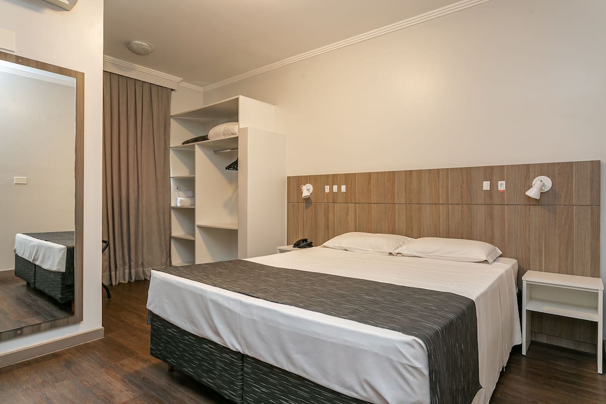 Una habitación de hotel moderna con una cama grande, una mesita de noche, un armario y un espejo.