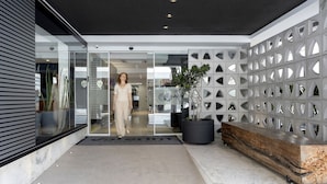 Una entrada moderna de edificio con puerta de vidrio, un banco negro y una planta en maceta.