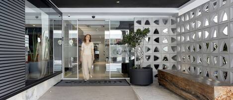 A modern building entrance with a glass door, a black bench, and a potted plant.