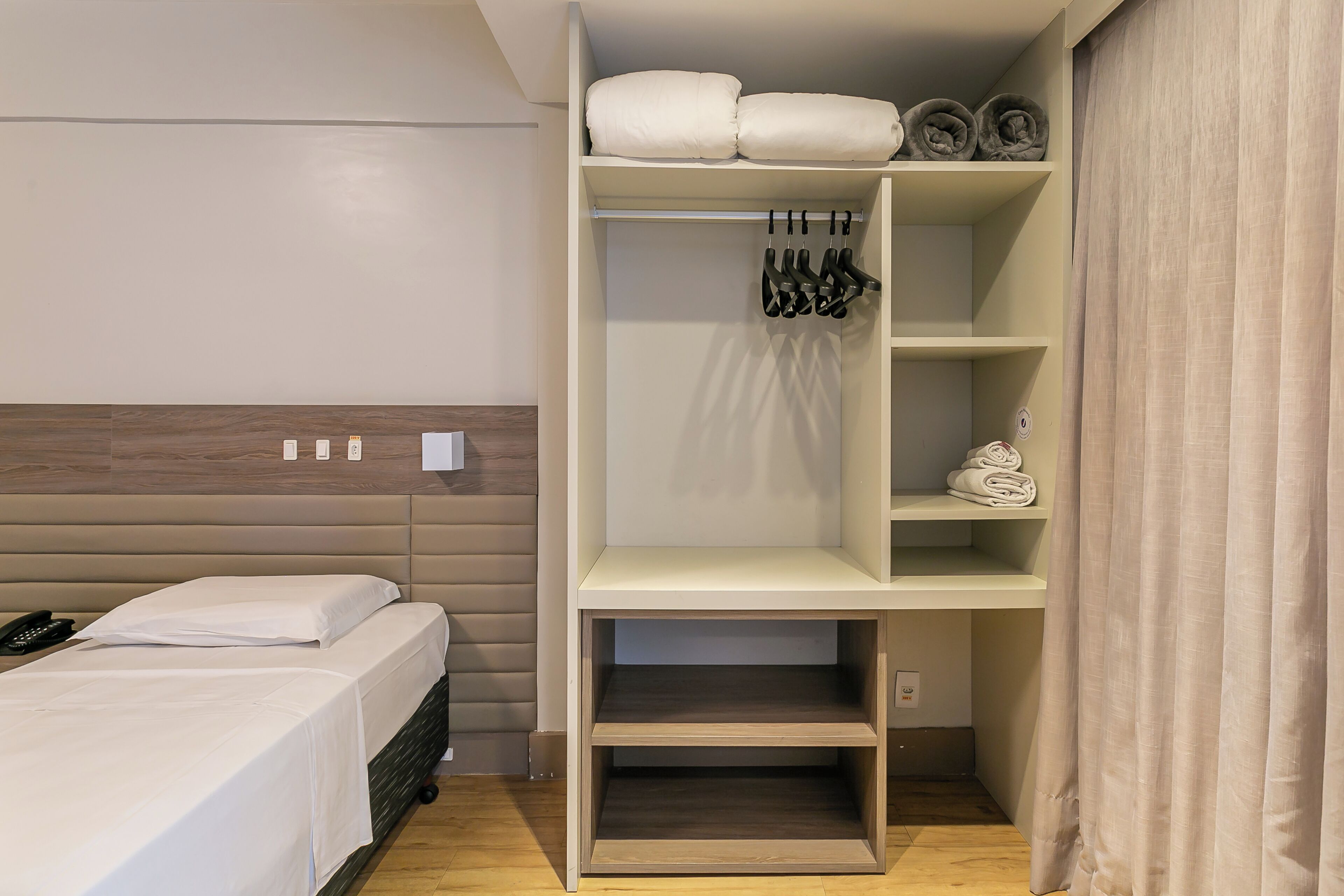Habitación de hotel con cama, armario con ropa colgada y estante con toallas dobladas.