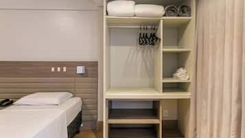 Habitación de hotel con cama, armario con ropa colgada y estante con toallas dobladas.