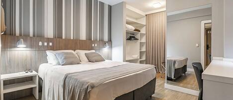 Una habitación de hotel moderna con una cama grande, mesitas de noche, un armario y un escritorio.