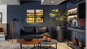 Una sala de estar moderna con una pared azul oscuro, un sofá de cuero negro, una mesa de centro de madera y una planta grande en maceta.