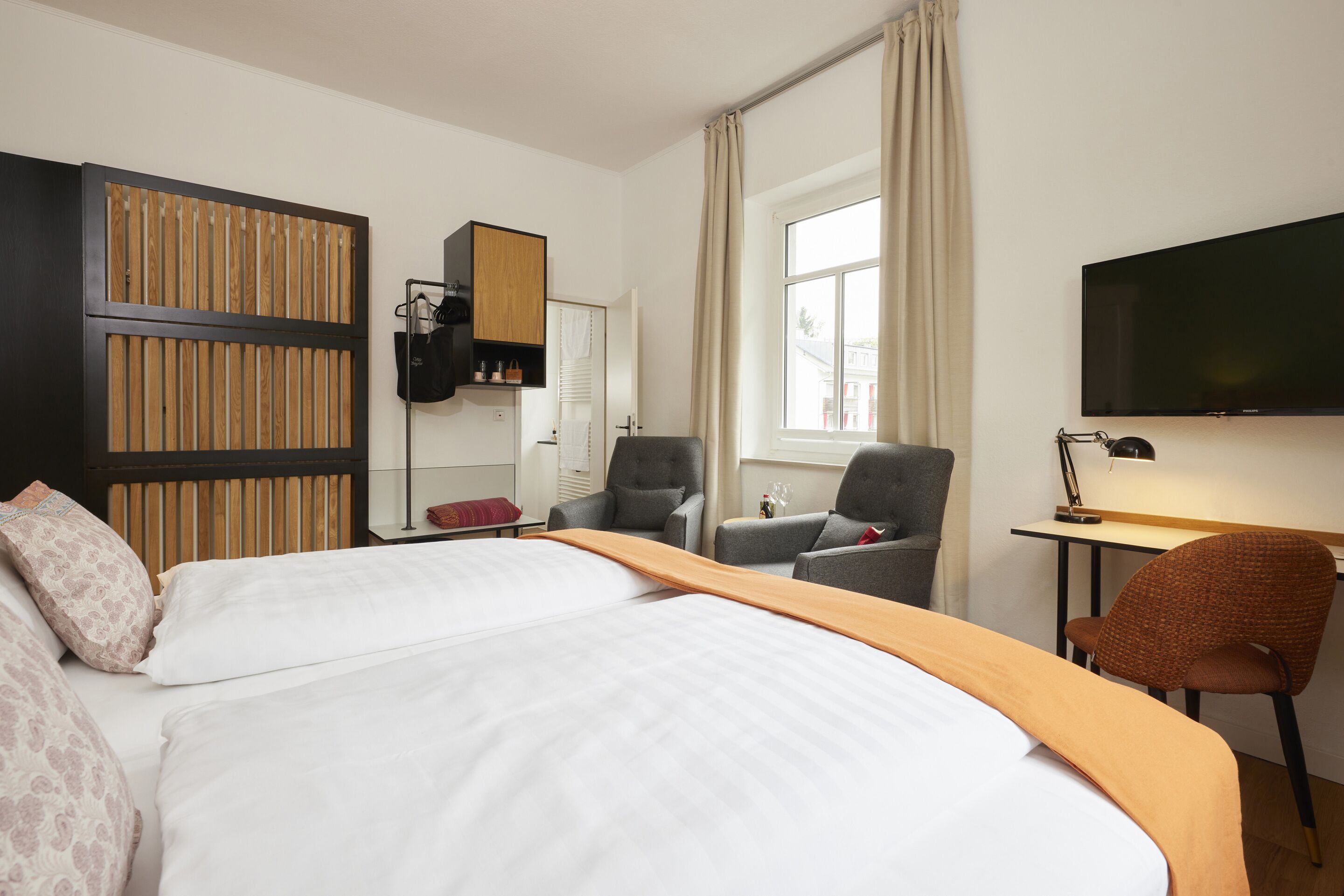 A hotel room with a bed, a desk, a chair, a wardrobe, a television, and a window.