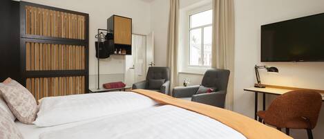 A hotel room with a bed, a desk, a chair, a wardrobe, a television, and a window.