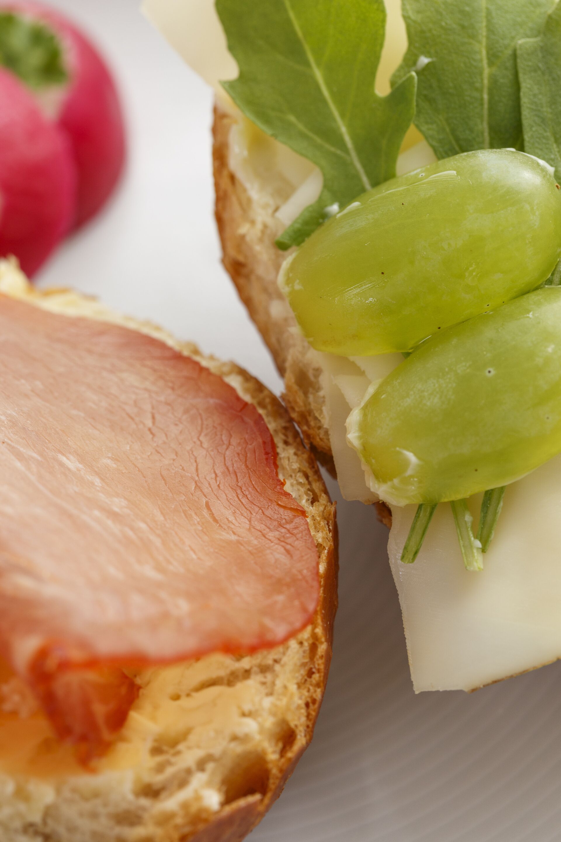 A sandwich with ham and cheese on a slice of bread, accompanied by a bunch of green grapes and a radish.