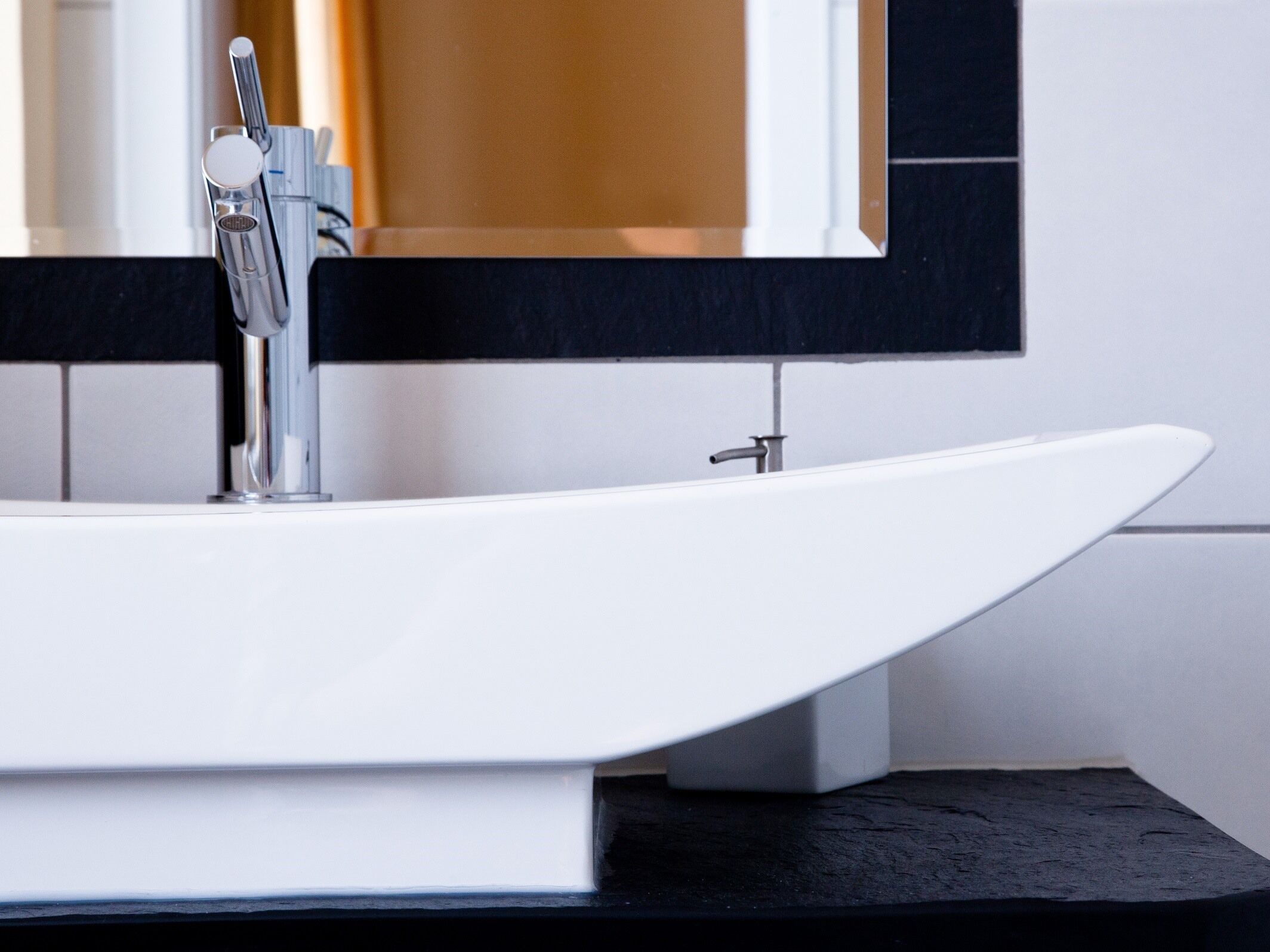 A modern bathroom with a white freestanding sink, a chrome faucet, and a black countertop.