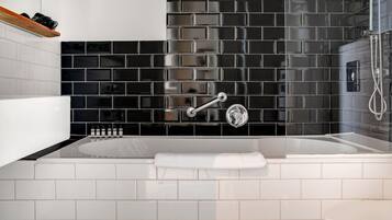 Een moderne badkamer met een wand betegeld in zwart en wit, een witte badkuip en een douchehoek.