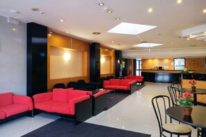 Un vestíbulo de hotel con sofás rojos, un mostrador de recepción y un reloj en la pared.