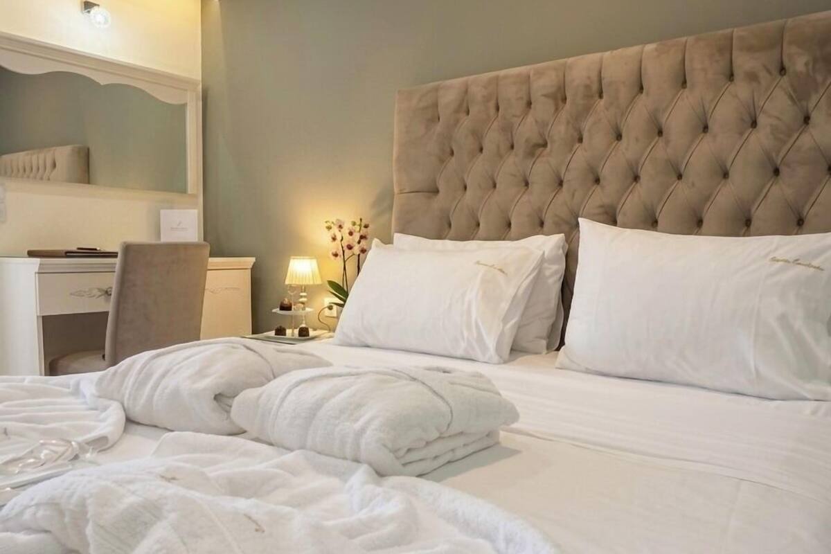 A neatly made bed with white linens, a tufted headboard, and a bedside table with a lamp and a small plant.