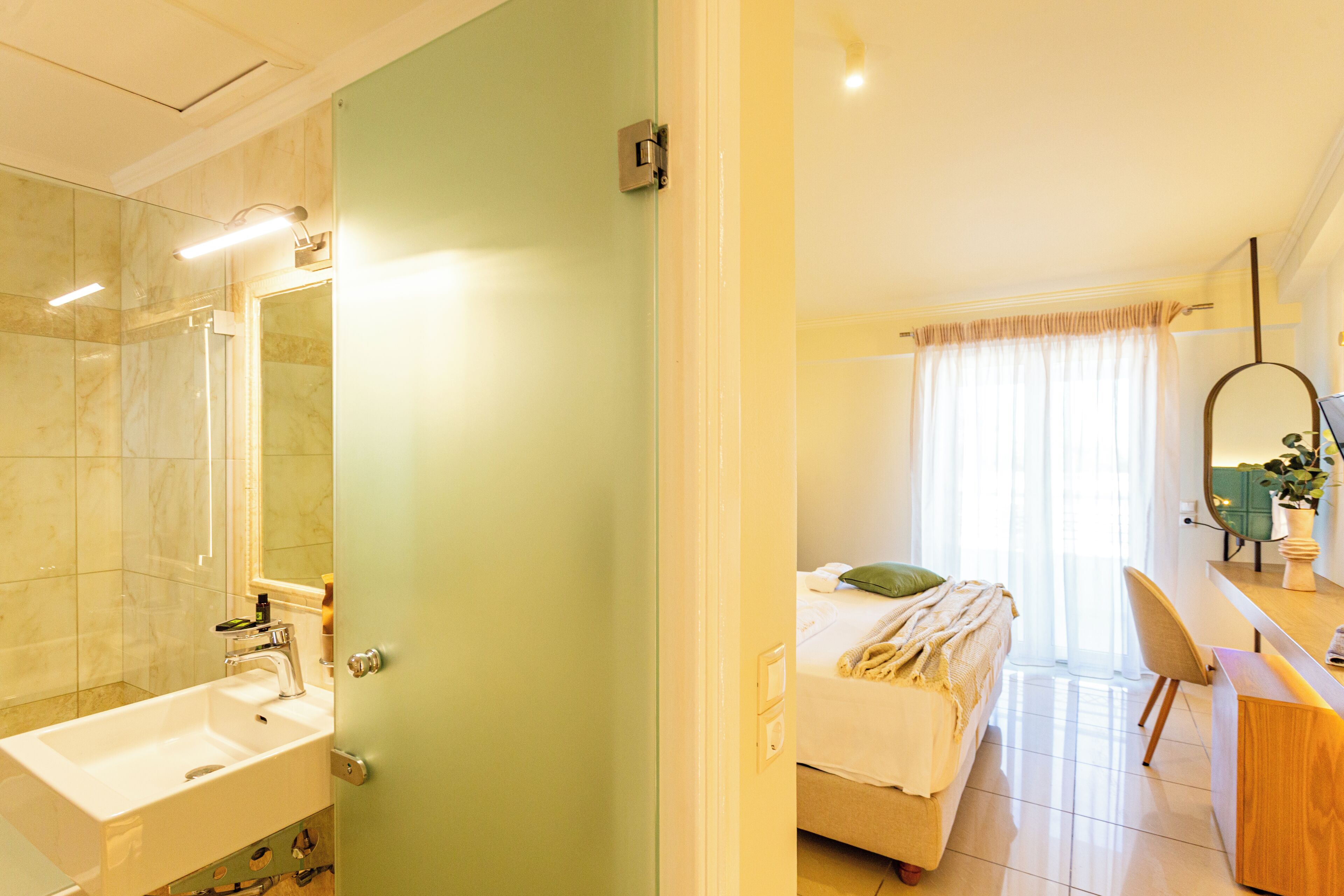 A hotel room with a bathroom, a bed, a desk, and a mirror.